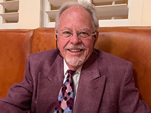 a man with white hair and white facial hair sits in a chair facing the camera