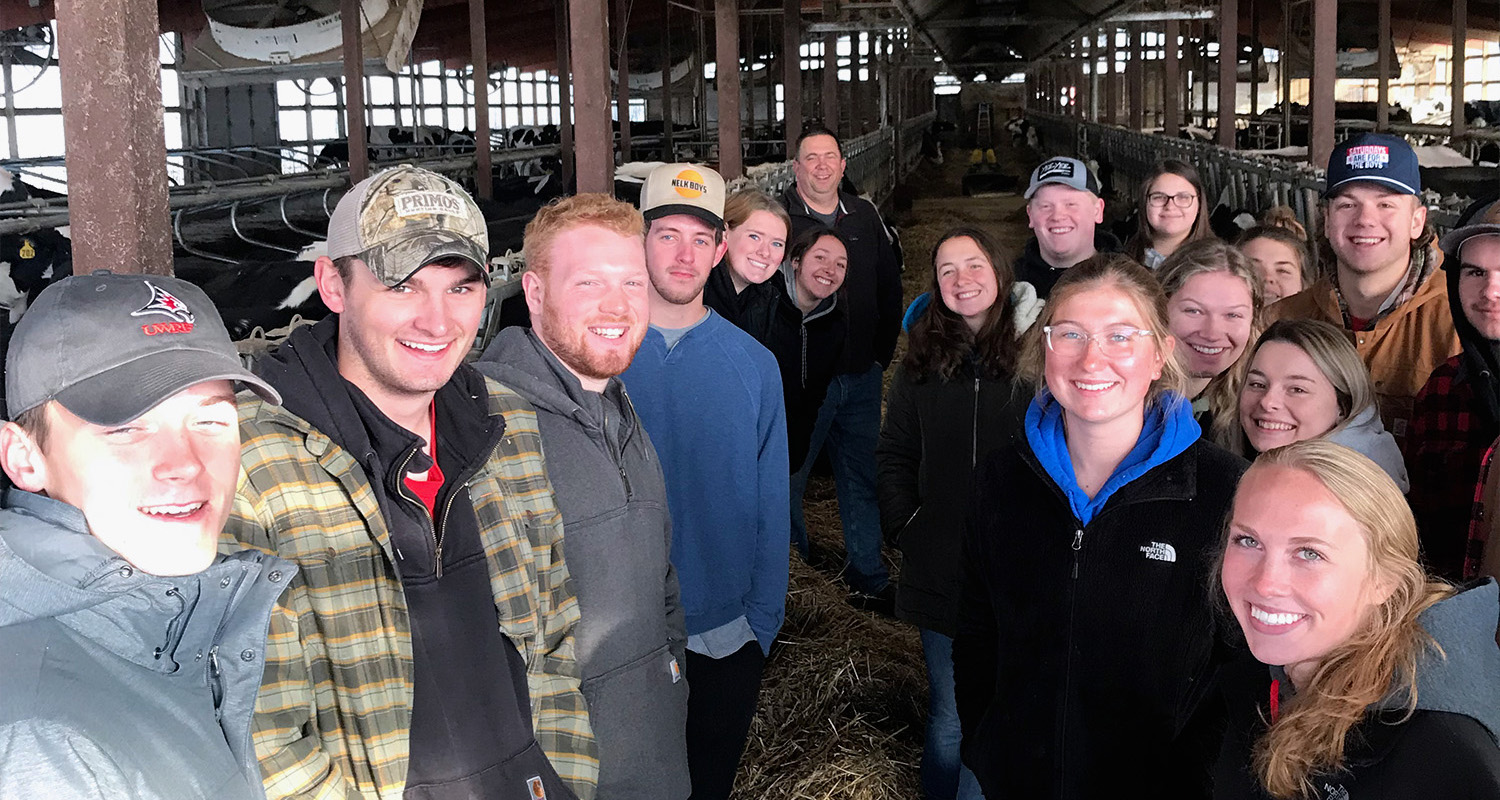 A group of agricultural business students stand in a barn at Mann Valley Farm