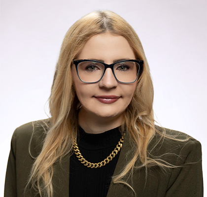 Headshot of Alicia Reinke-Tuthill, a woman with long blonde hair and black glasses wearing a green blazer