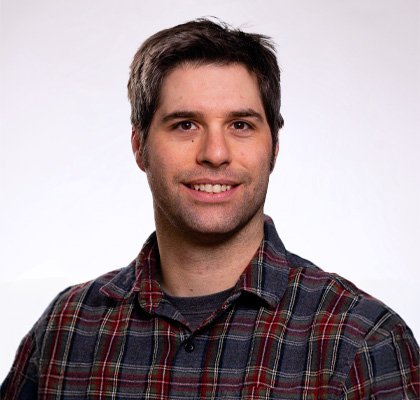 Headshot of Andrew Haveles. A man with short brown hair wearing a brown and red plaid button up.