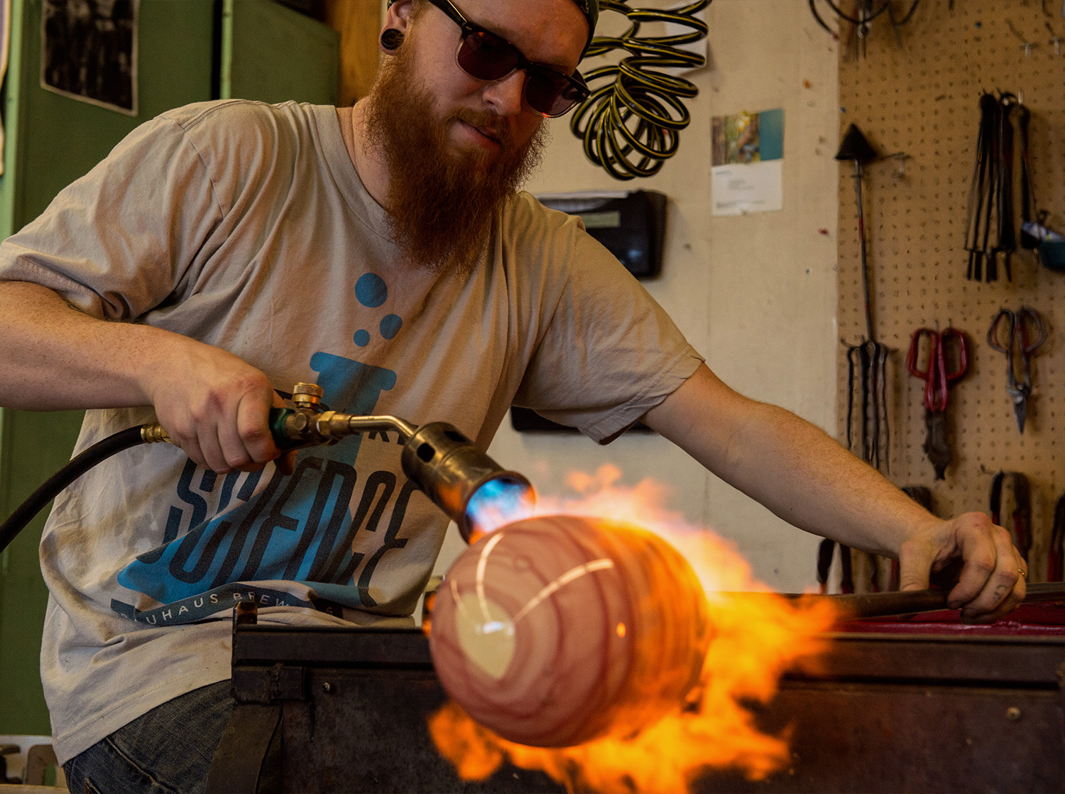 A male student blows flame on a glass piece in the glassblowing studio