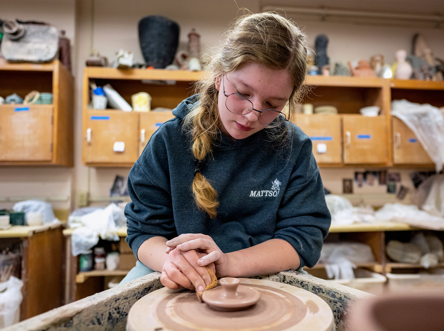 A female student sits at a pottery wheel working on a ceramic piece
