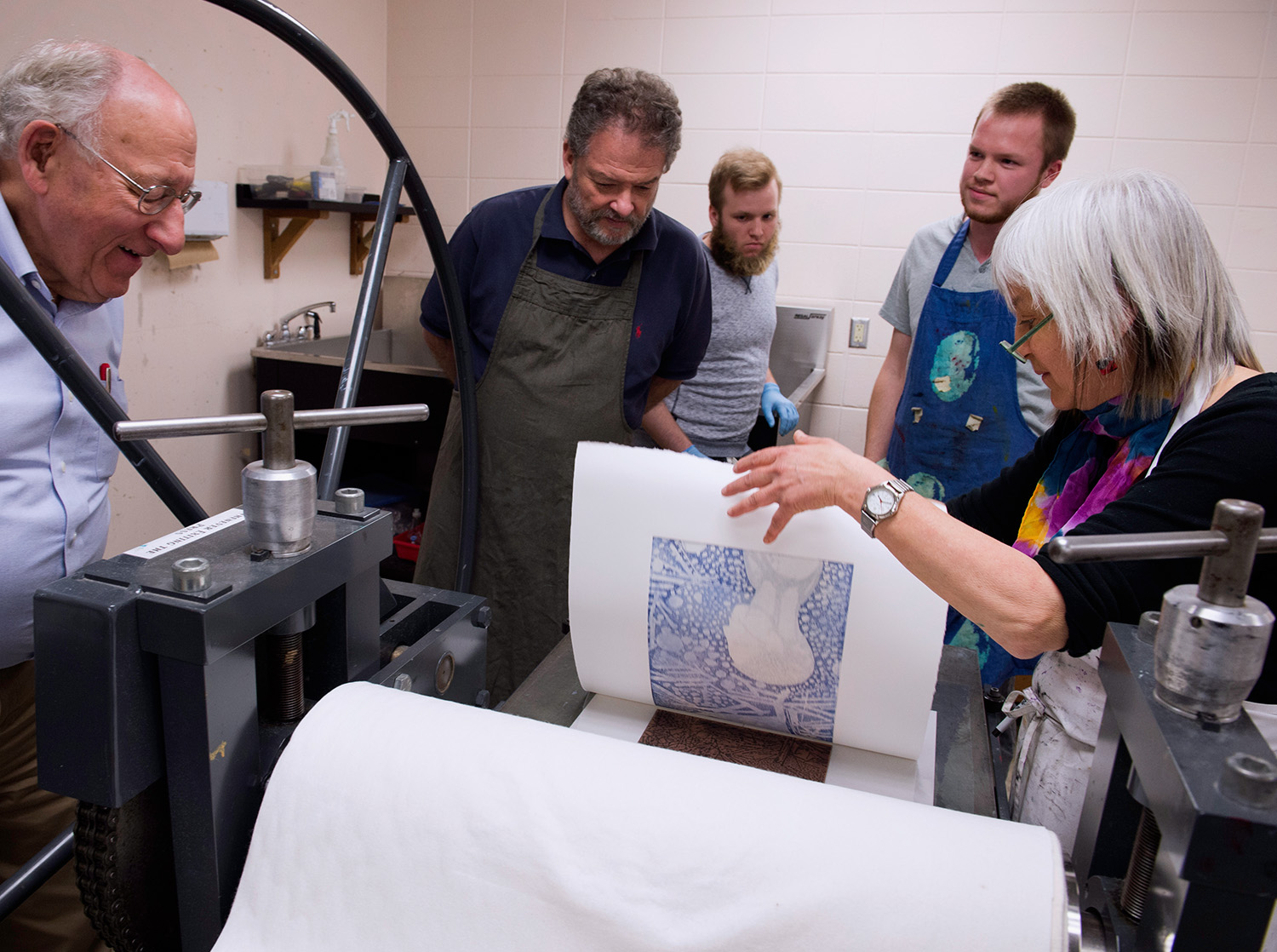 Multiple people stand over a printmaking press while one person pulls a print