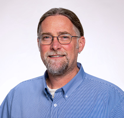 Headshot of Benjamin Crain, a middle aged man with brown and grey hair, glasses and a blue striped button down shirt