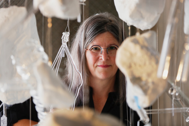 Beth Lipman peering through her hanging glass sculpture.