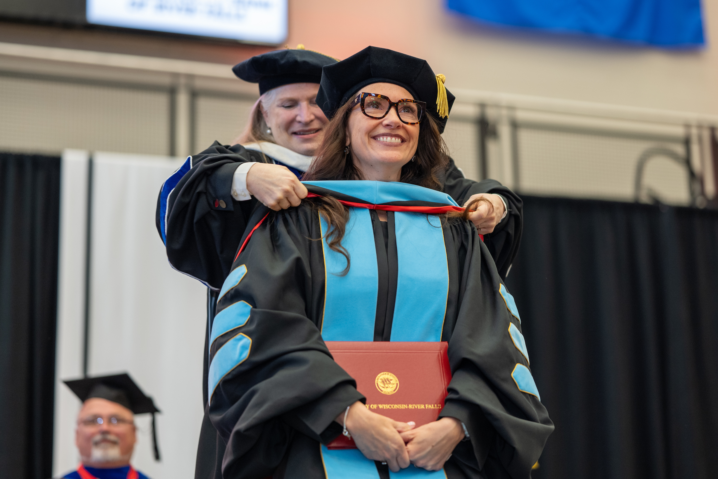 a student receives a doctoral hood from a faculty member at commencement