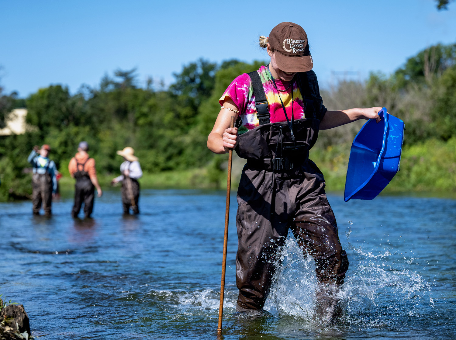 A female student walks through the Kinnickinnic River in waders during a science class