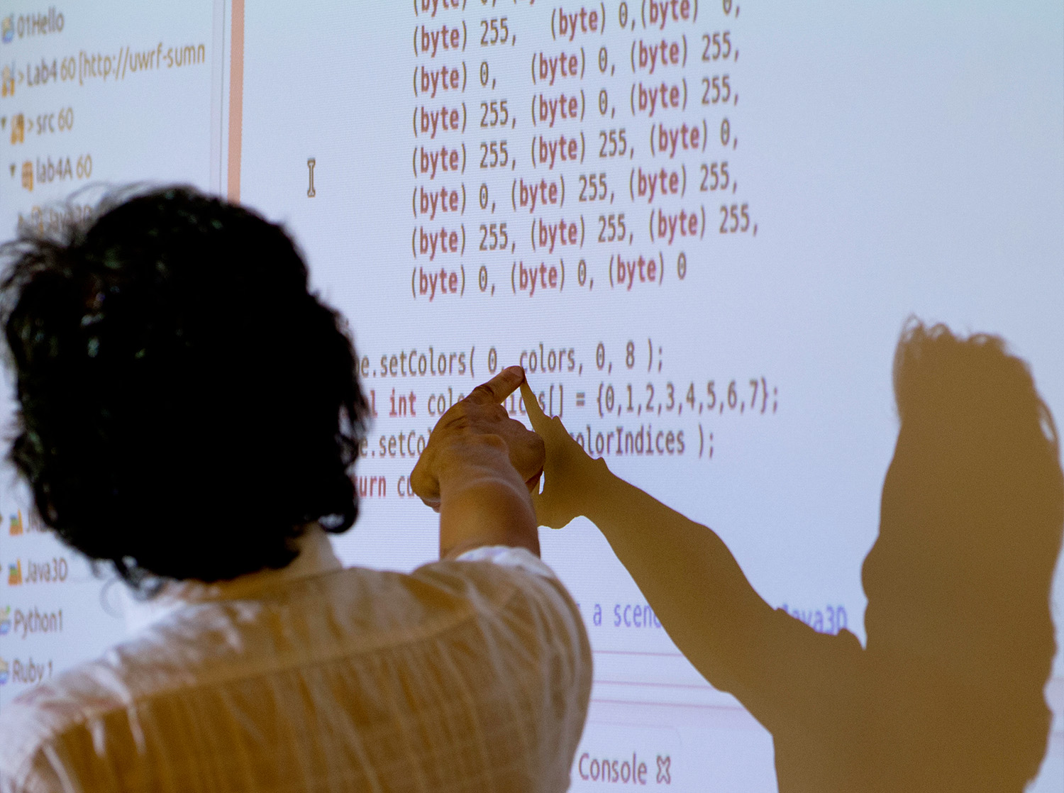 A student points to computer code projected on a whiteboard