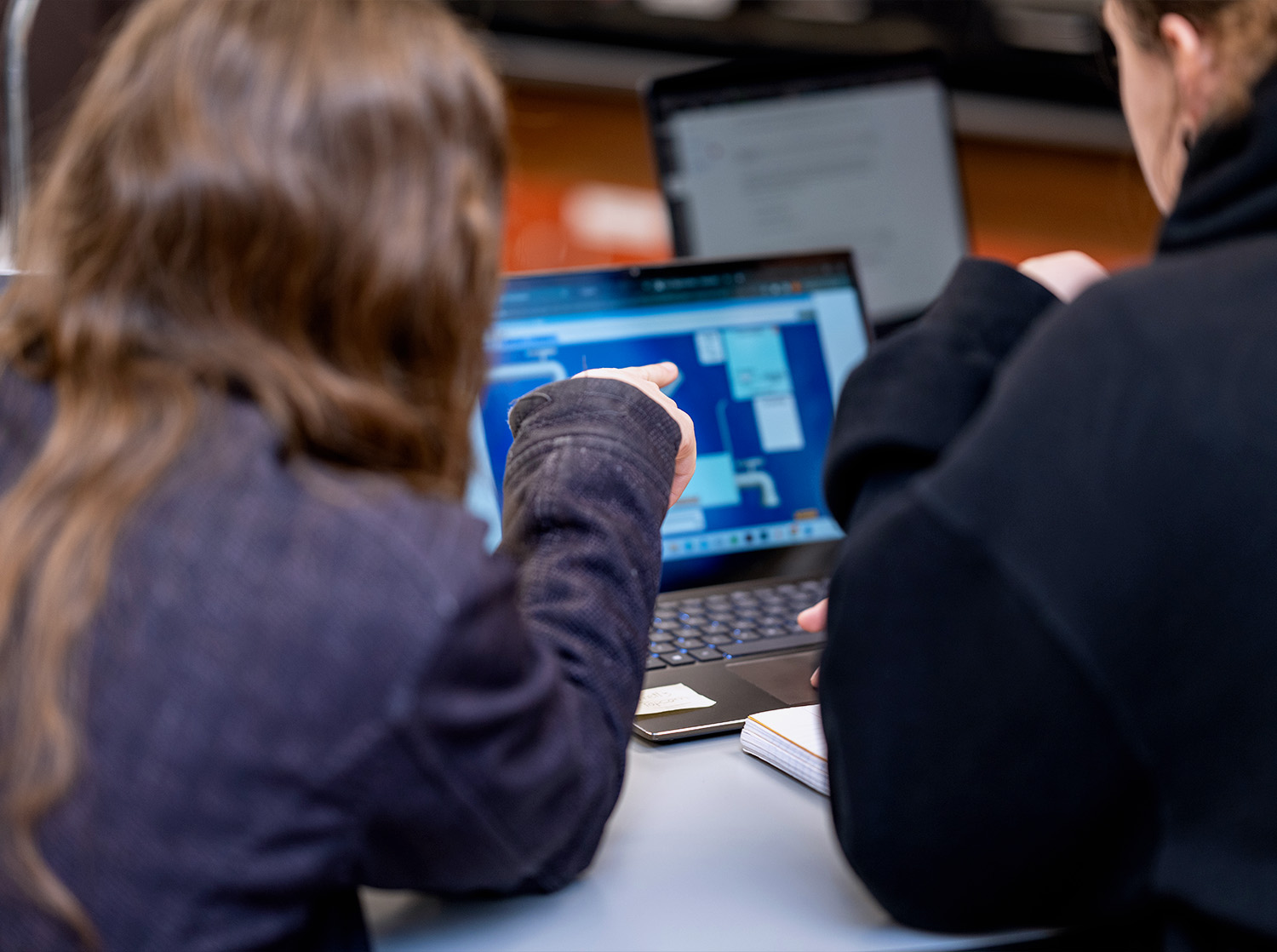 A professor points at information on a students laptop