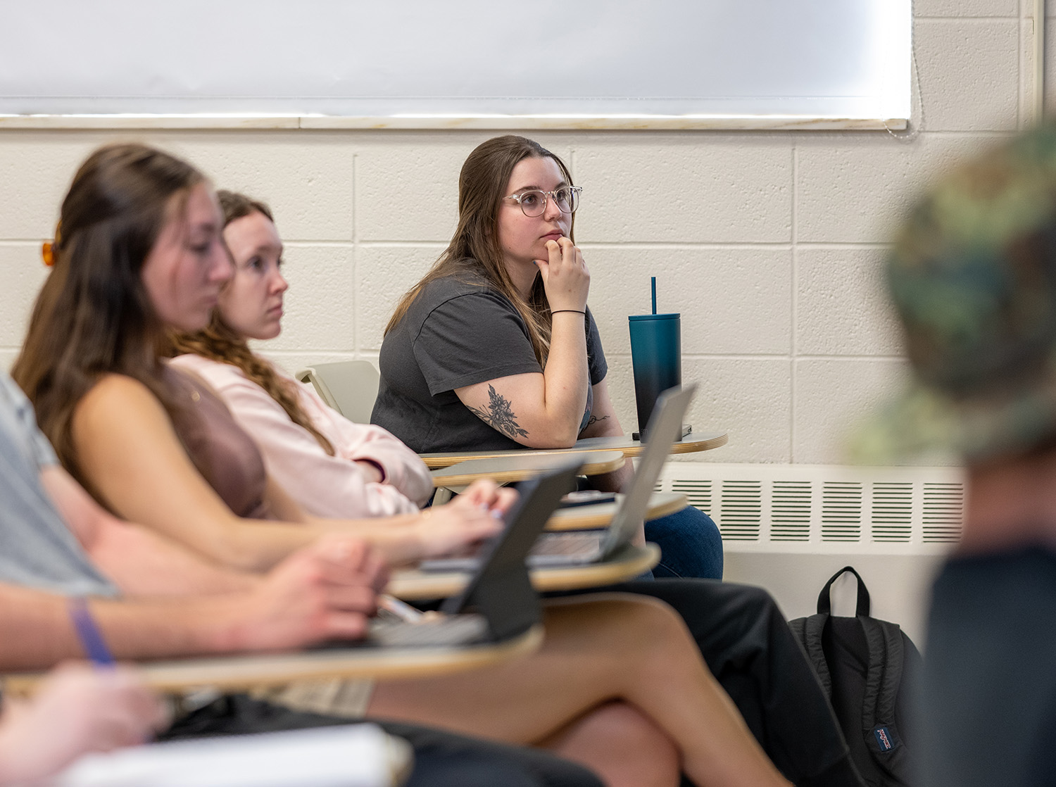 A female student sits at a desk listening to the speaking professor