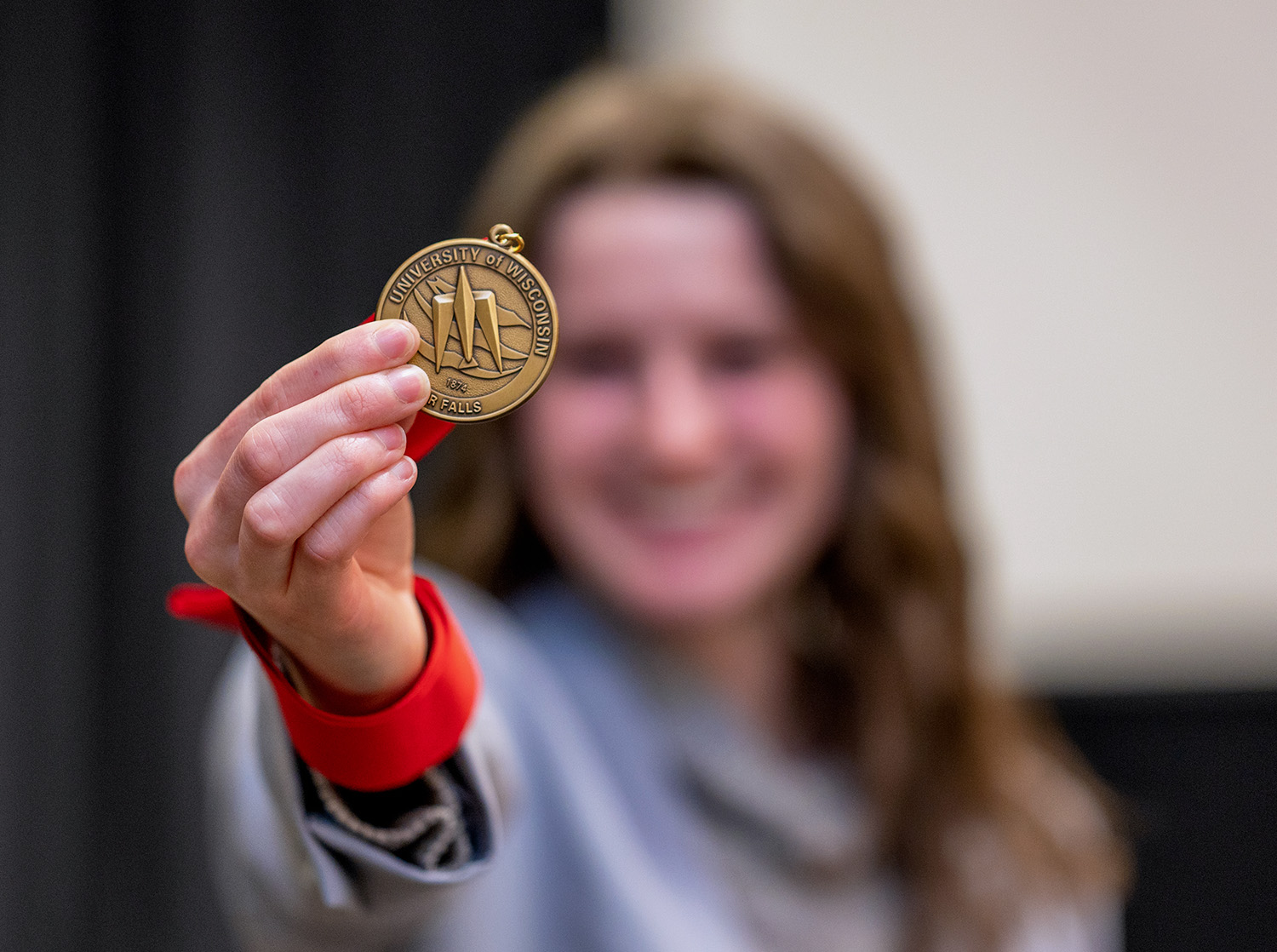 A female student holds a medal out to the camera