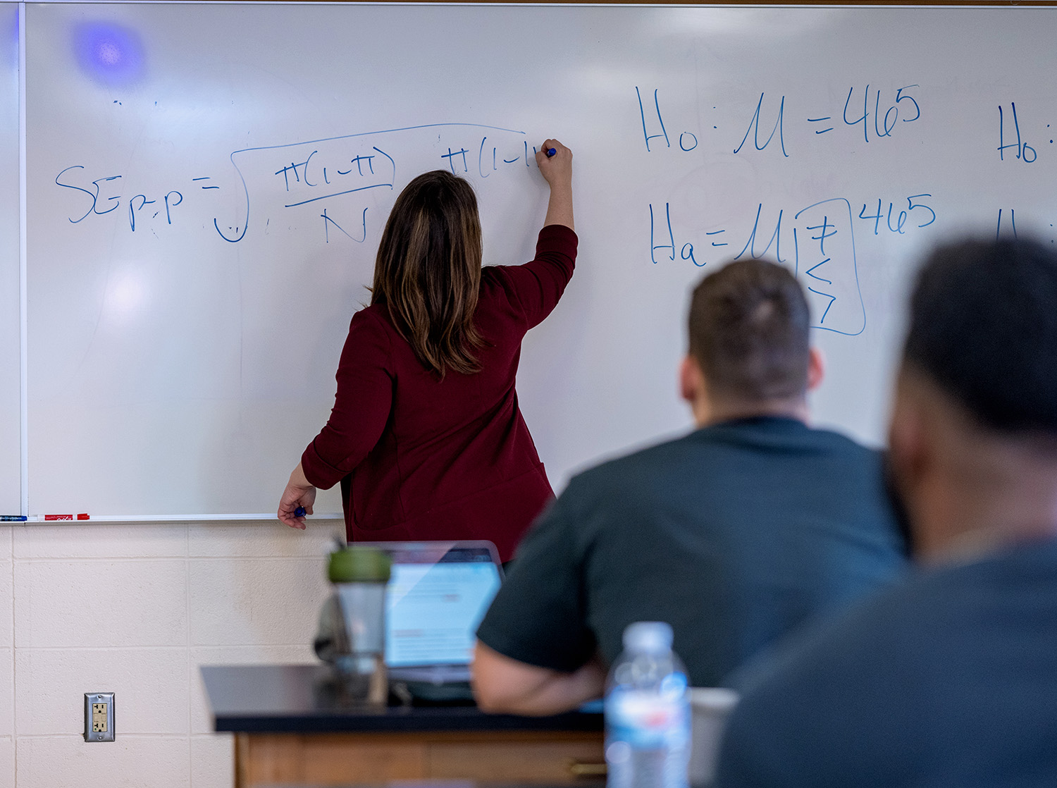 A female professor writes an equation on a whiteboard