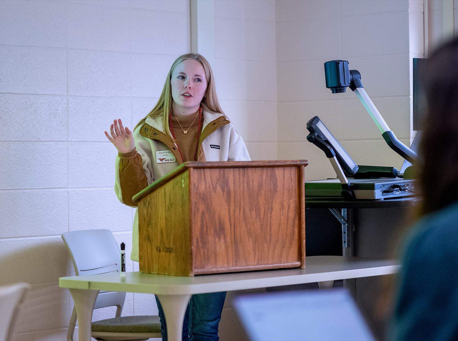 A female student stands behind a podium giving a senior thesis presentation to the class