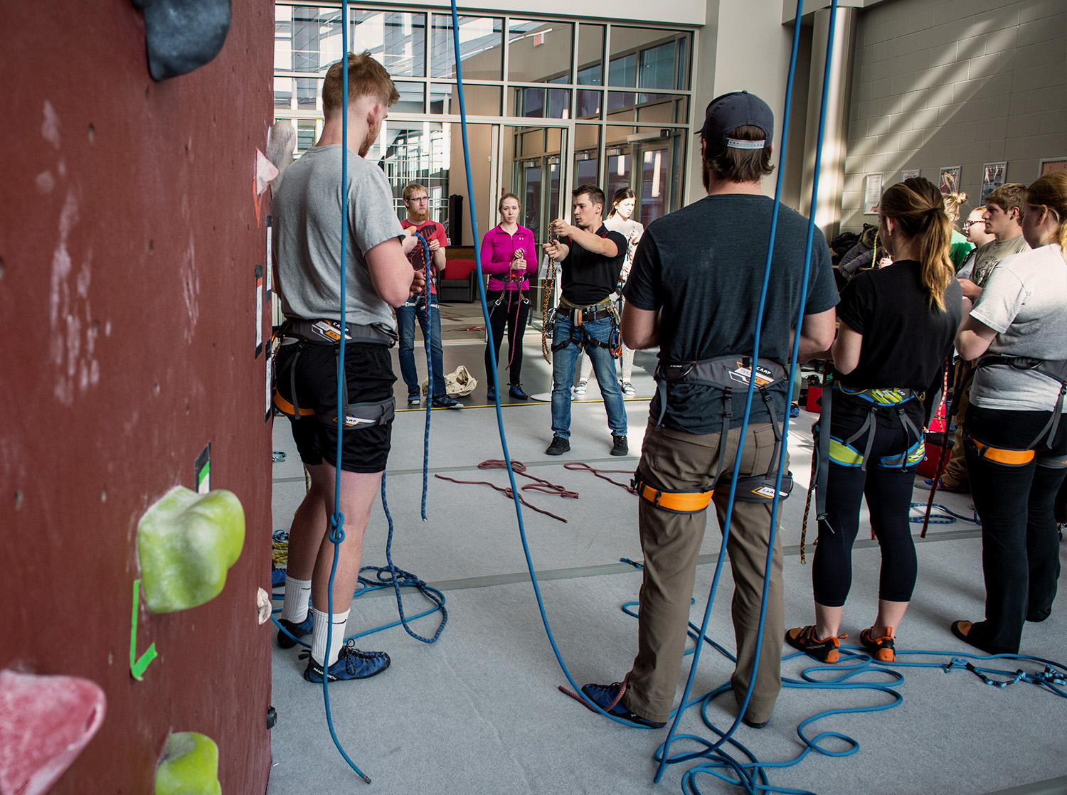 A group of students listen to a climbing instructor standing in the climbing wall in the Falcon Center