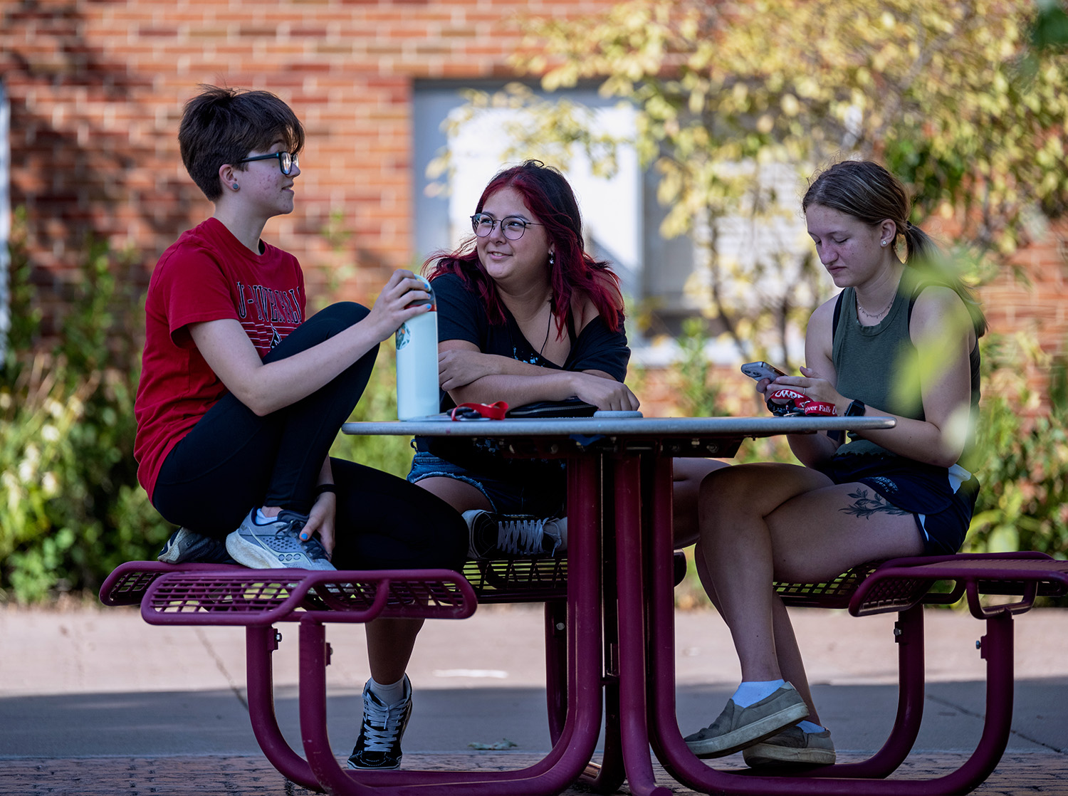 Three students sit on a table enjoying the weather outside