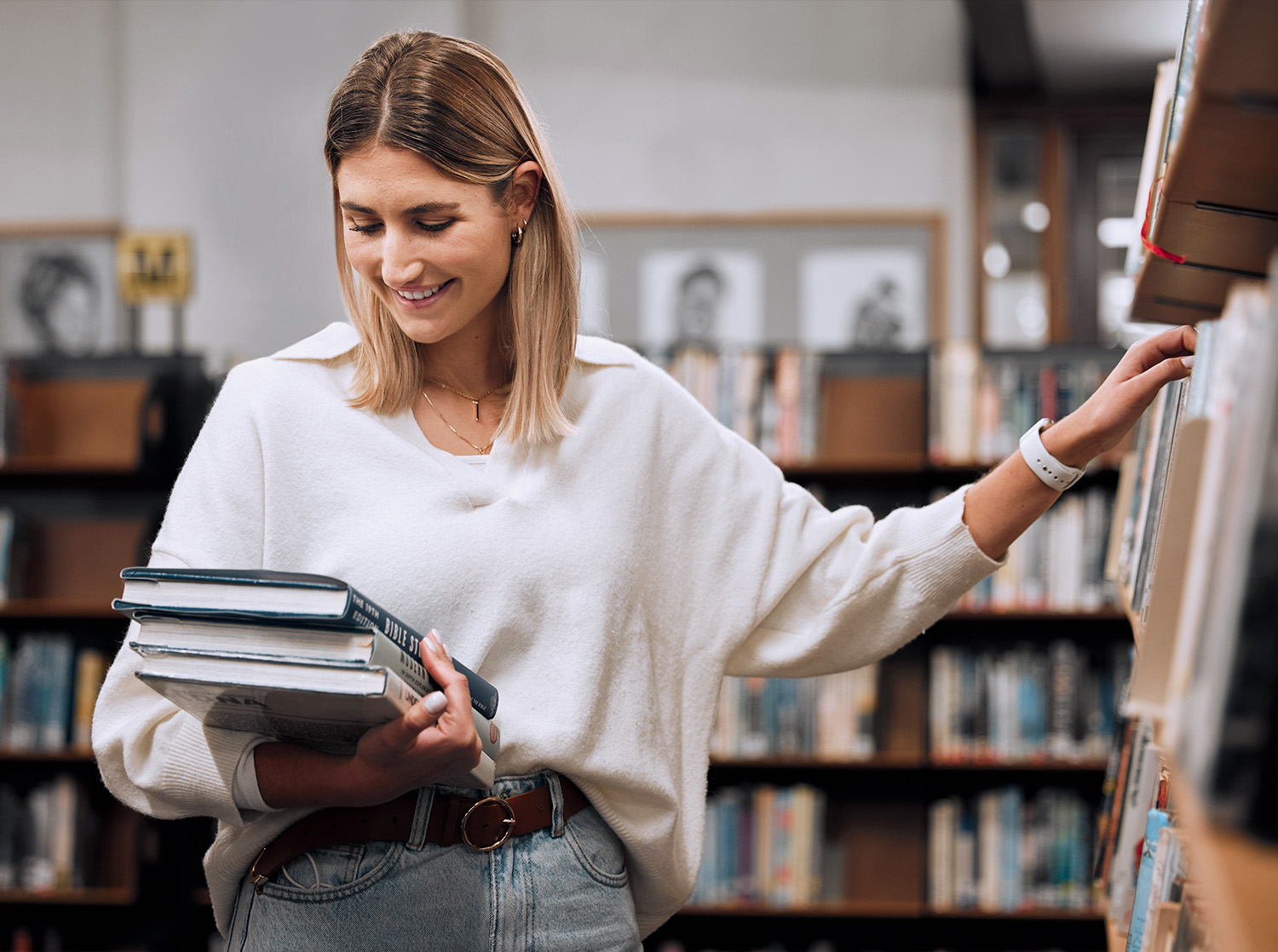 A female student holds library books and browses the shelves