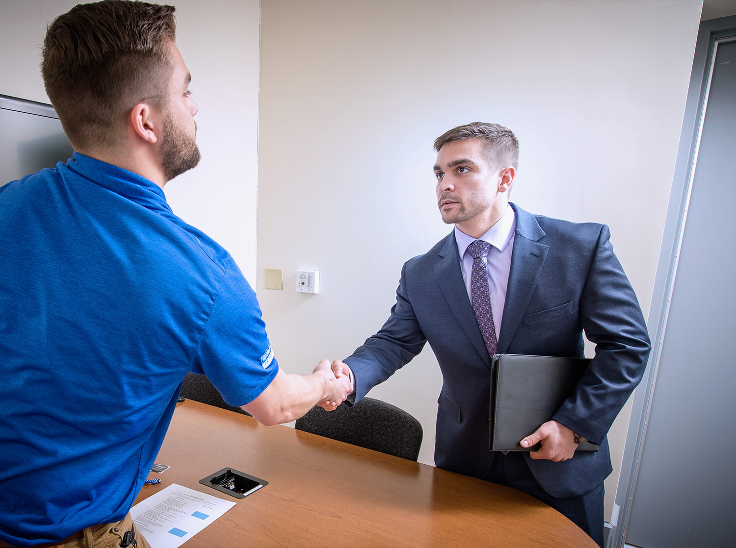 Two male students shake hands before they participate in a mock sales exercise