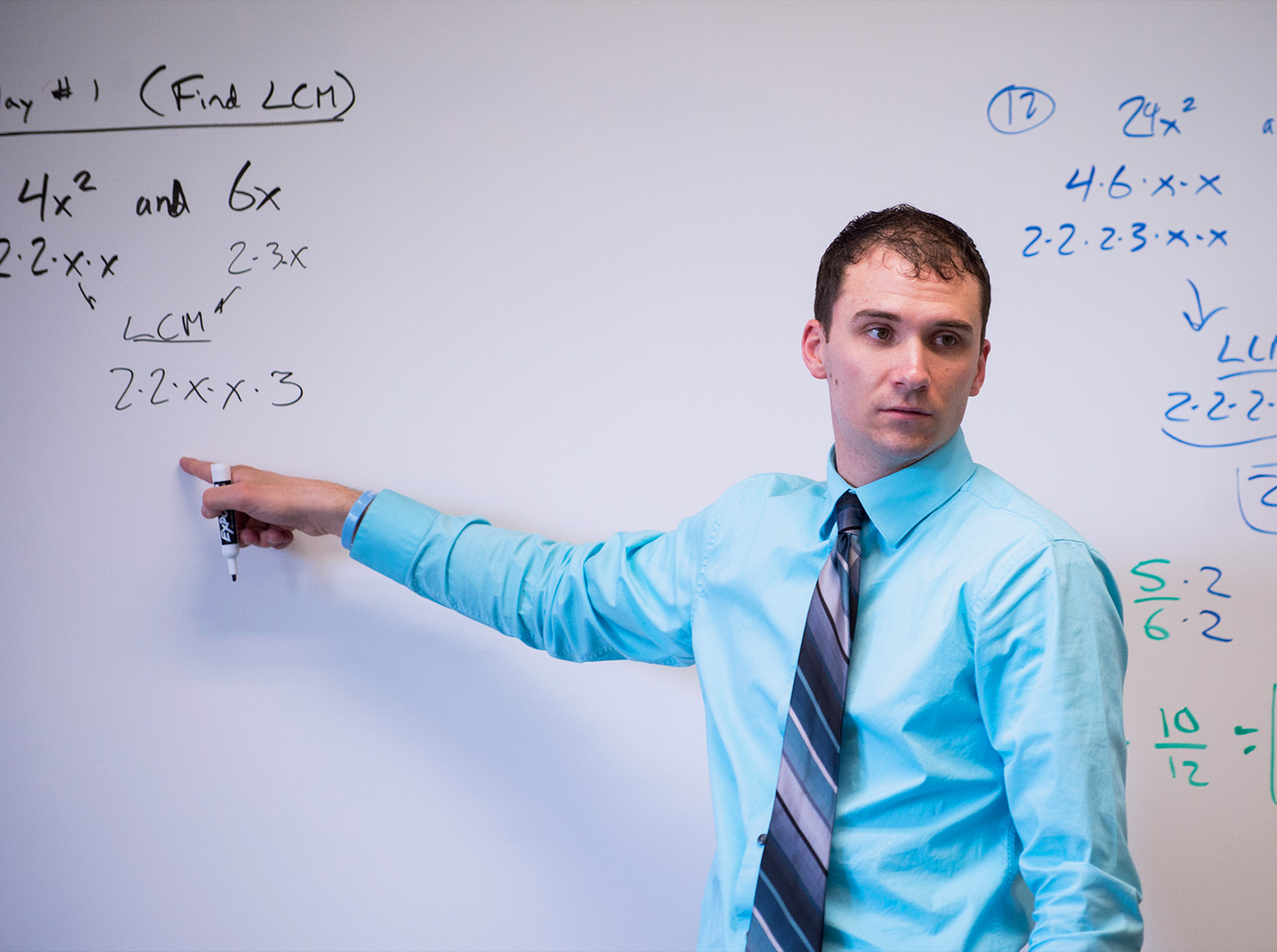 A male student teacher points at a math problem on the whiteboard