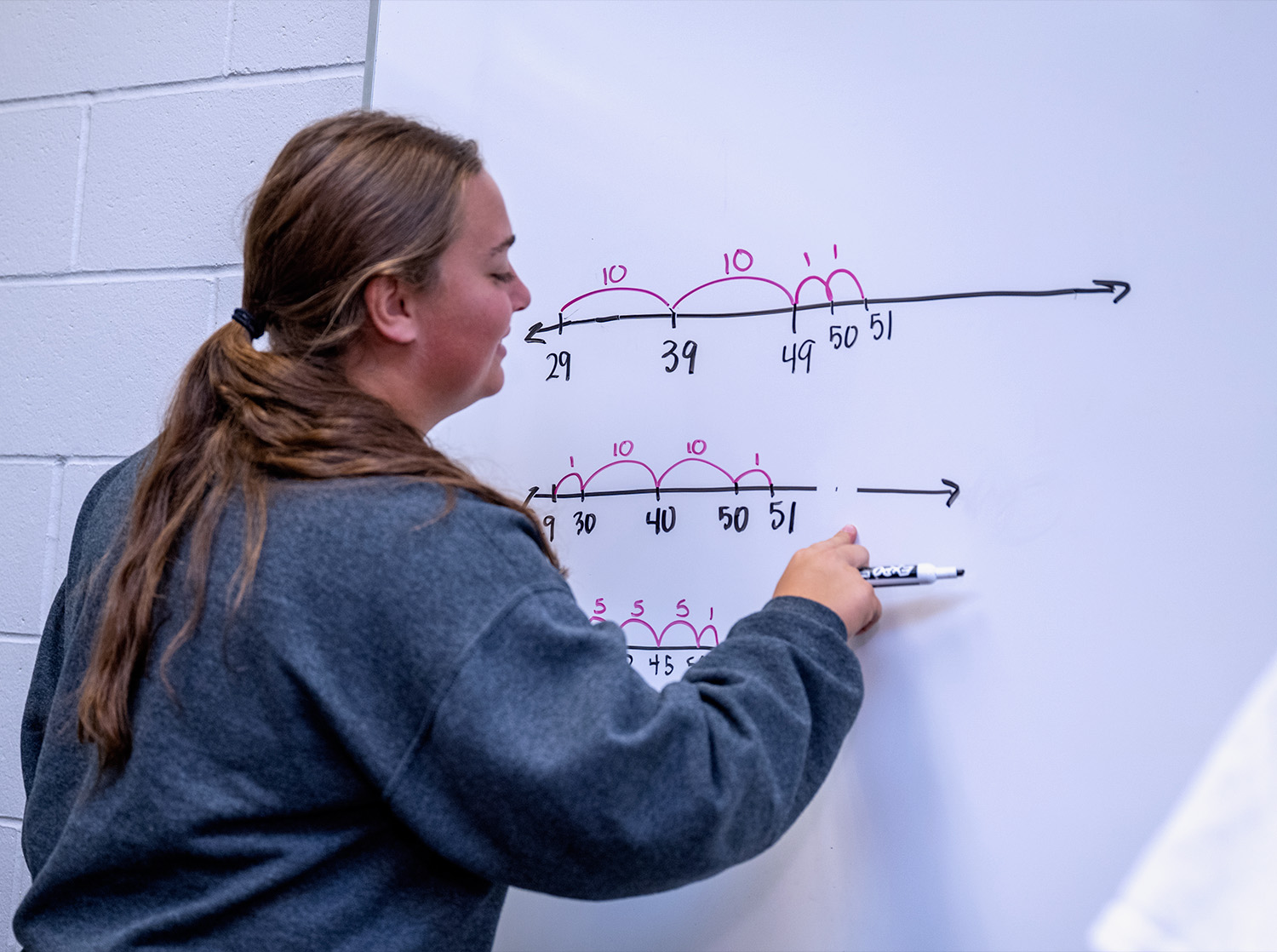 A female student writes a math problem on a whiteboard