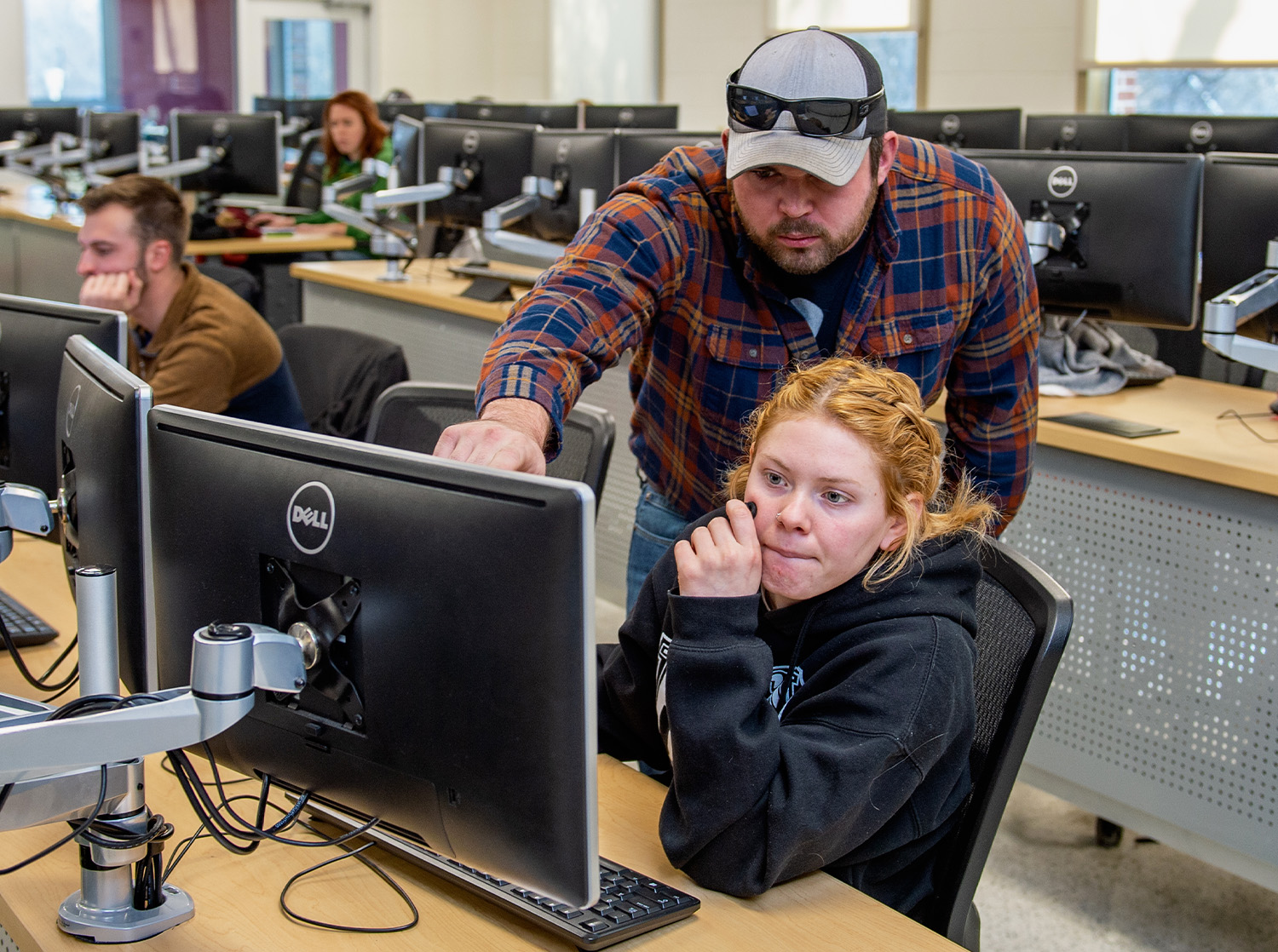 A tutor points to something on a computer screen while another student looks on