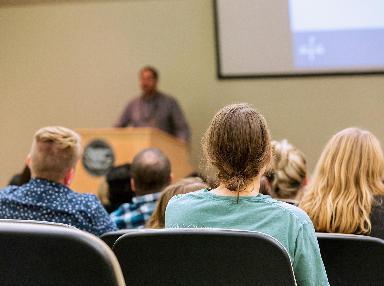 A group of students listen to a presenter at a podium