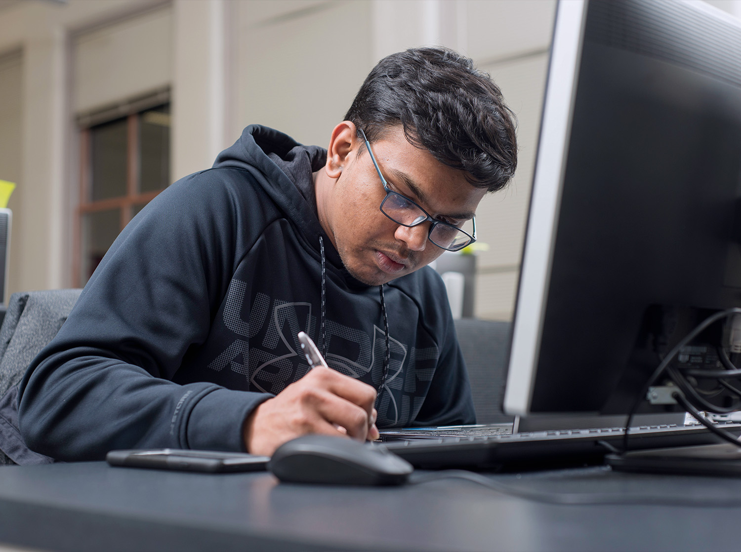 A male student sits at a desk writing in a notebook