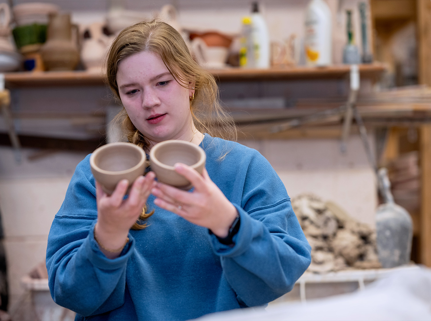 A female student compares two clay bowls in a ceramics class