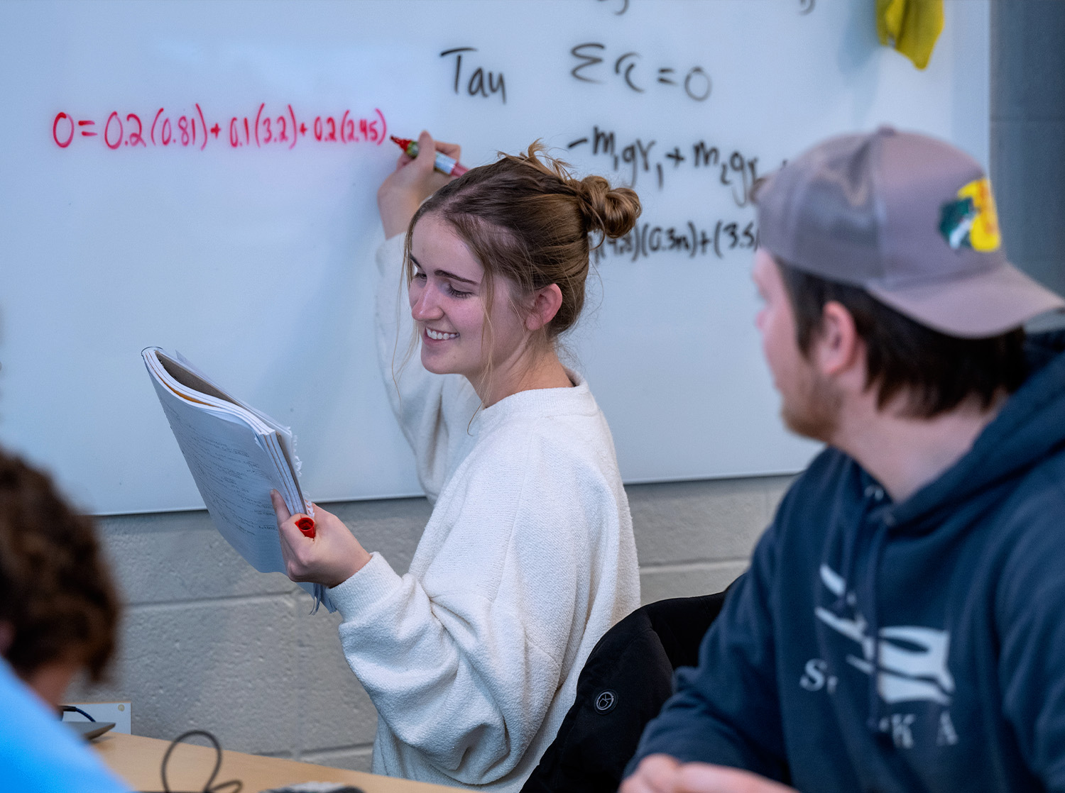 A female student writes a math equation on a whiteboard in class