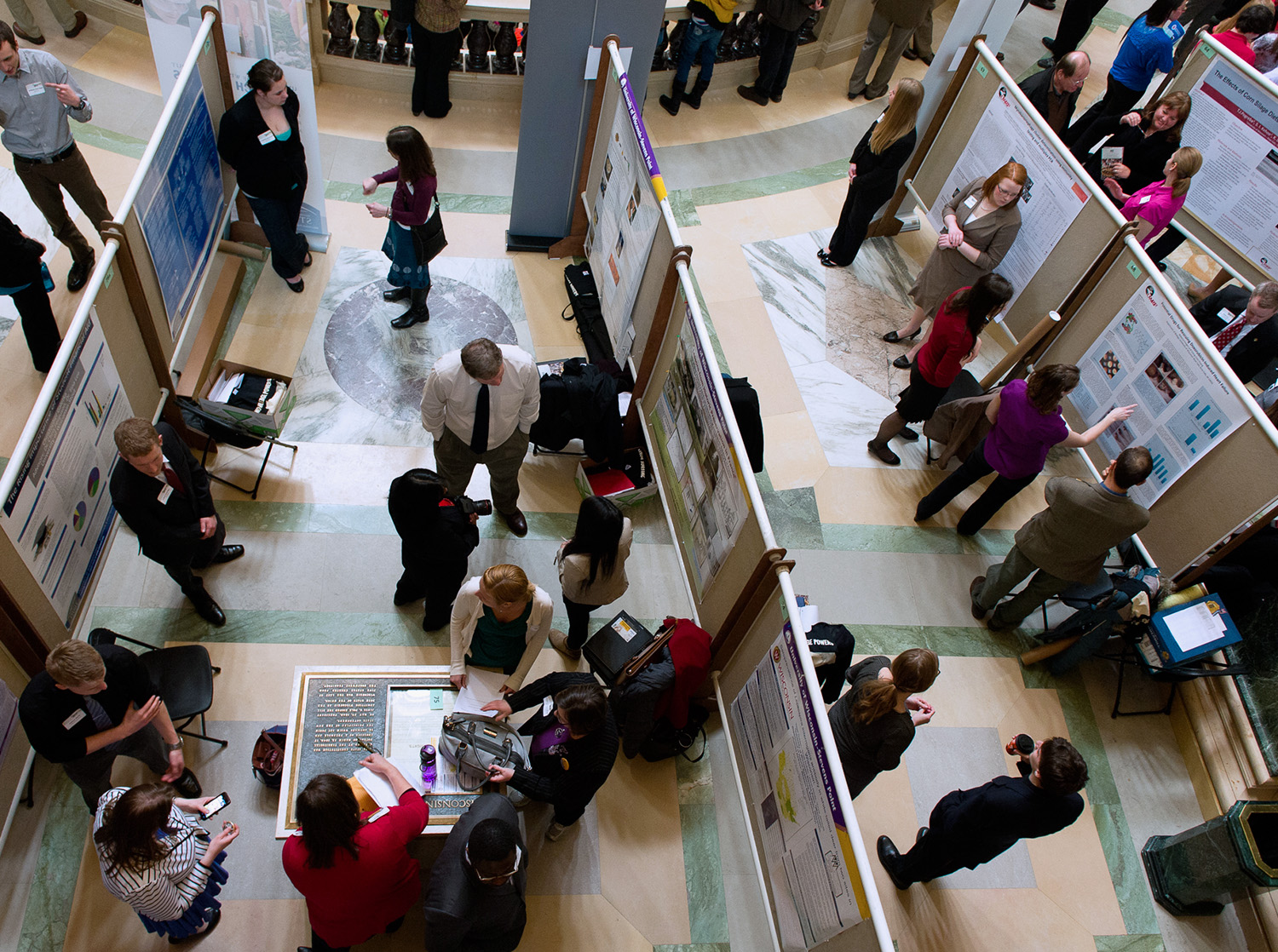 A group of people stand in the Madison State Capital building rotunda and present their research posters