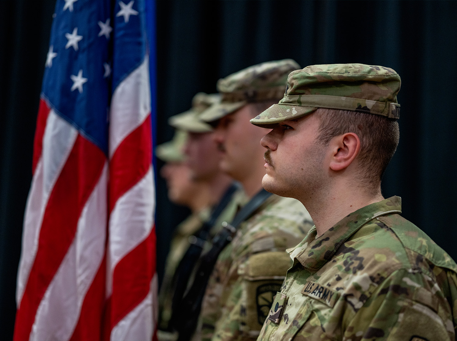 Military service member stand at attention holding flags during Commencement