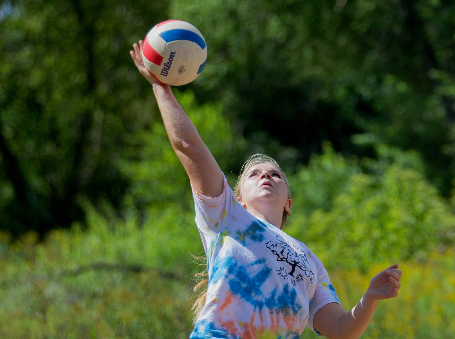 A student serves a volleyball during a sand volleyball tournament on campus