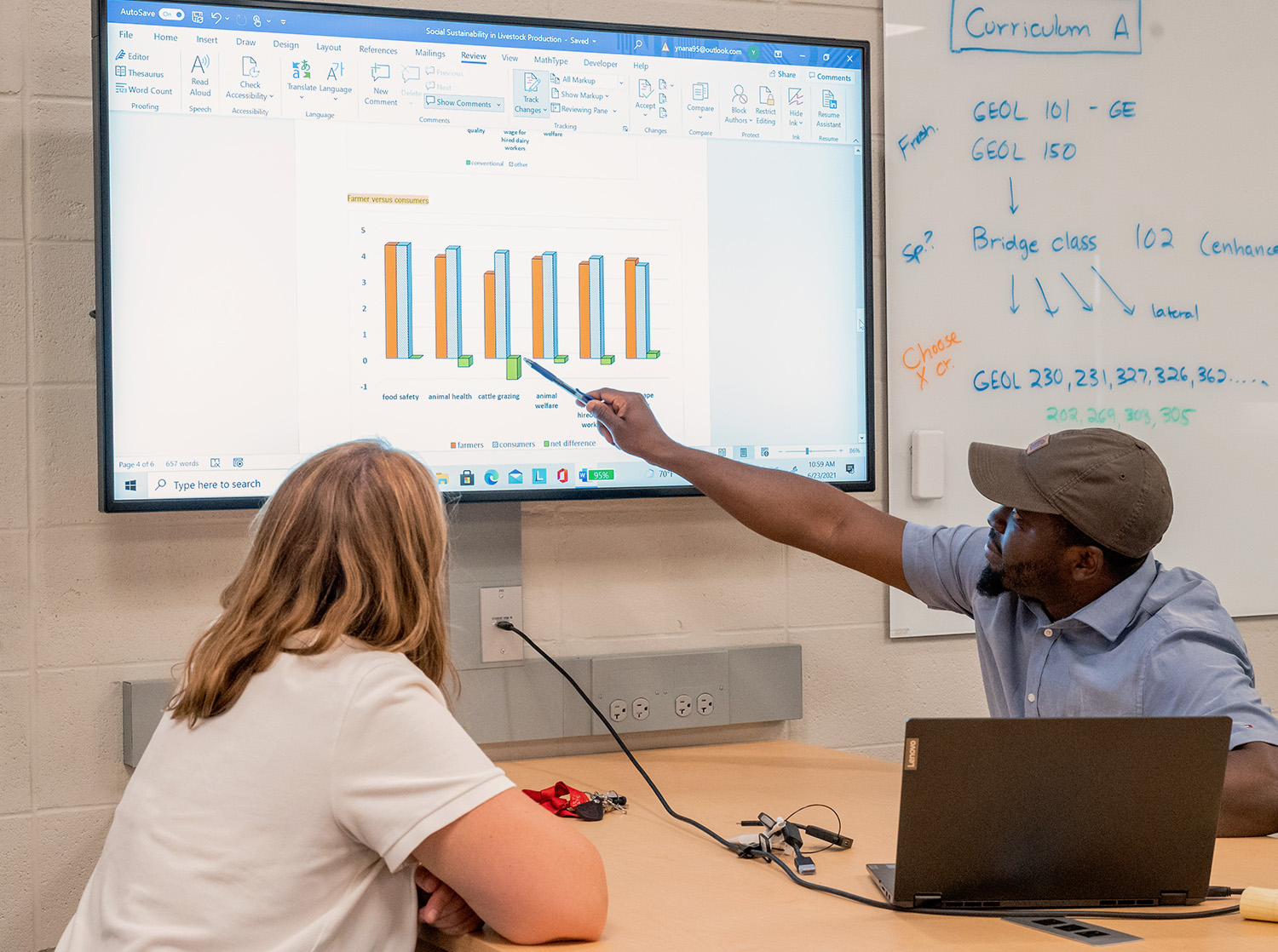 A professor points to a bar graph on a computer monitor