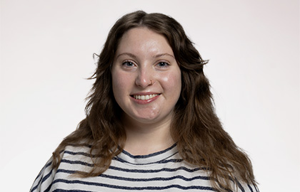 Headshot of Ciara Ferris, a young woman with long brown hair wearing a black and white striped shirt