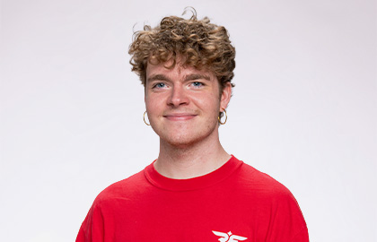 Headshot of Connor Montanya, a young man with short curly brown hair and hoop earrings wearing a red Residence Life shirt