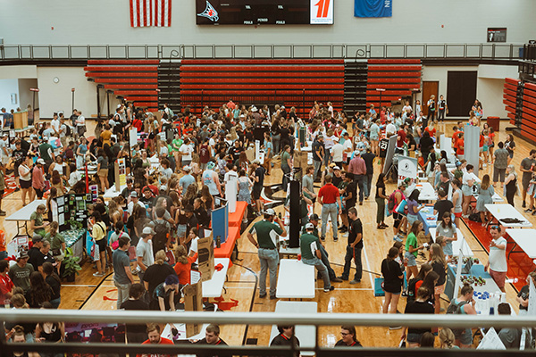 An overhead shot of a gymnasium filled with people visiting various booths. 