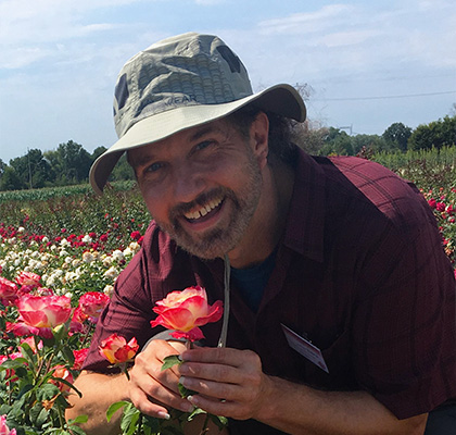 Headshot of David Zlesak, a man with black/gray hair wearing a hat holding a pink flower