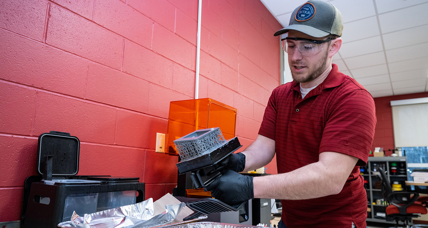 A male student inspects their 3D print in the 3D printing lab