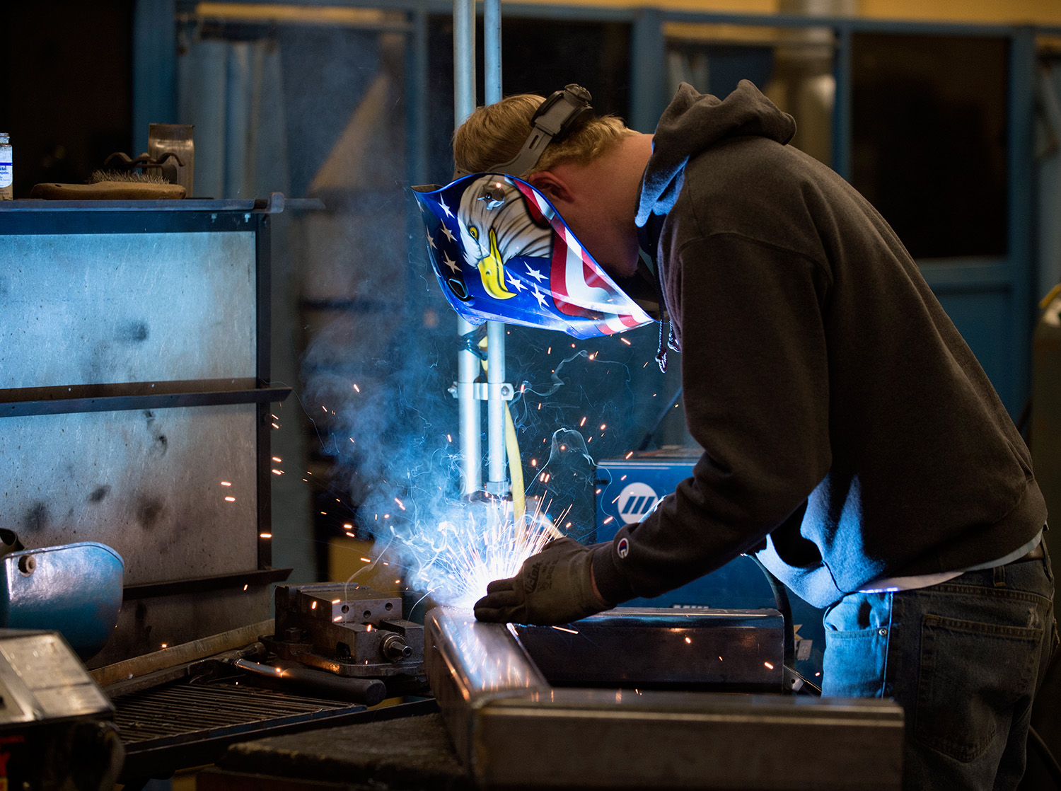 An engineering technology student welds two pieces of metal together in a shop