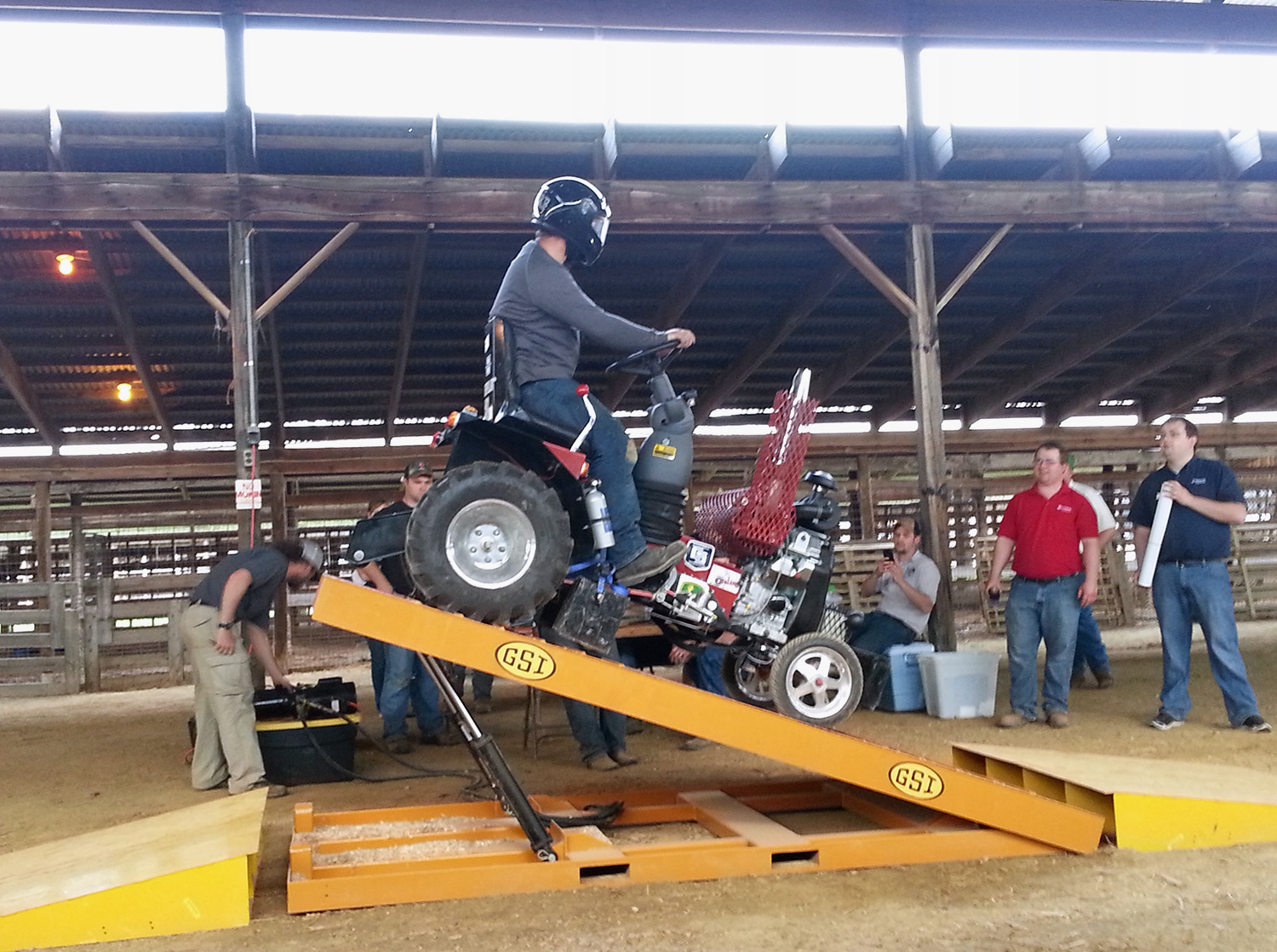 A male student sits on a small tractor on a ramp, ready for a race.