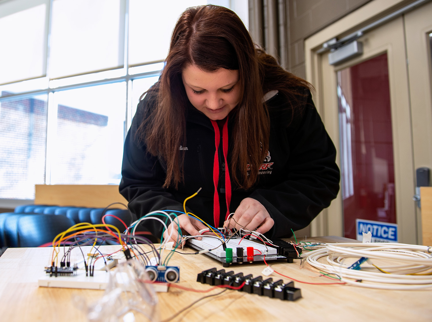 A female student connects electrical wires on a practice circuit board