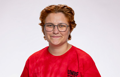 Headshot of Erin Besser, a young woman with short curly red hair wearing glasses and a red Residence Life shirt
