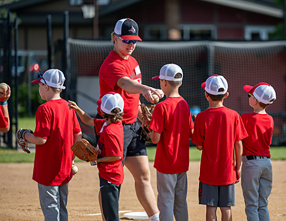 youth baseball players wearing red tshirts shake hands with a college baseball player