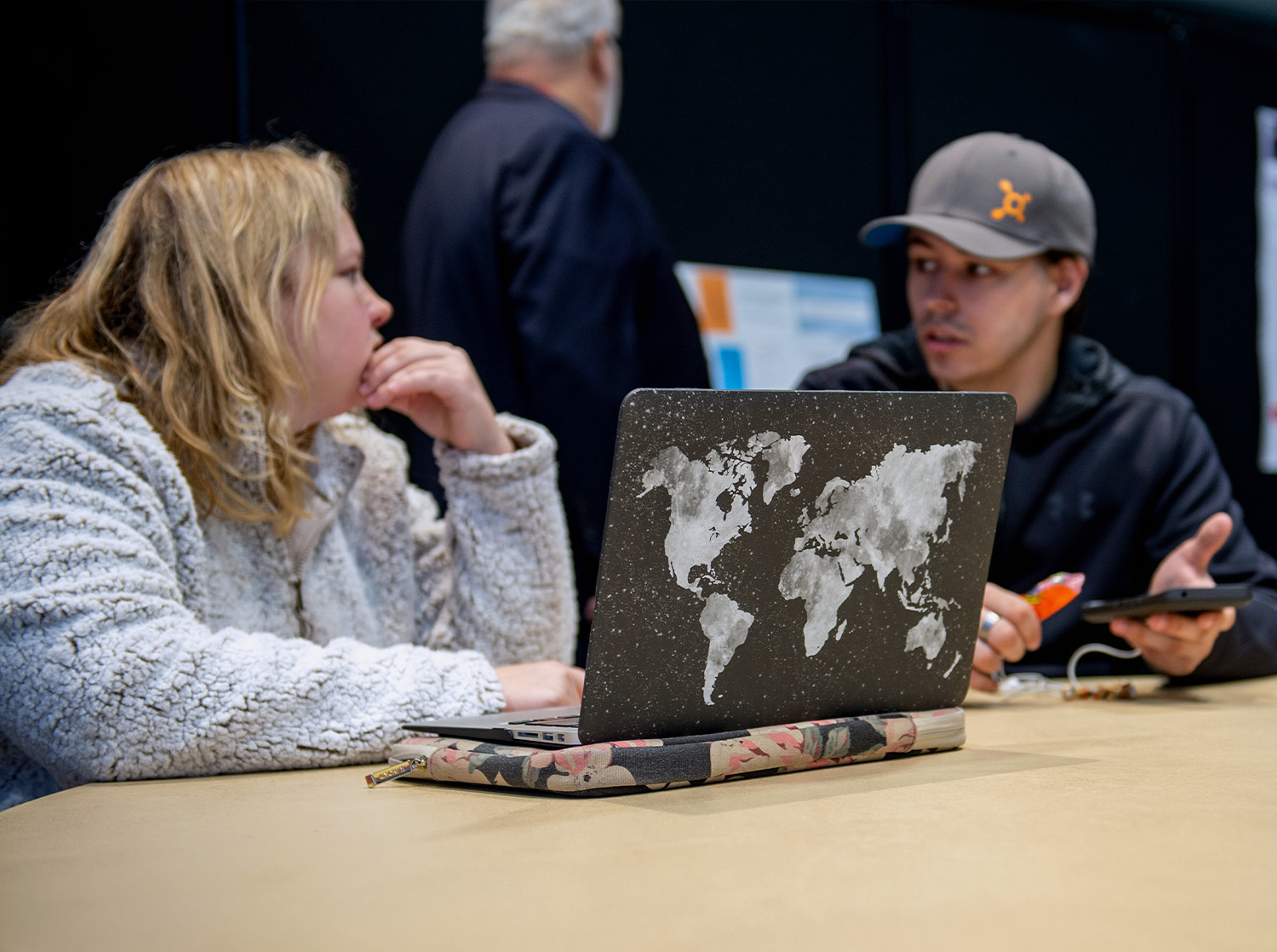 A male and female student talk with a laptop open facing them