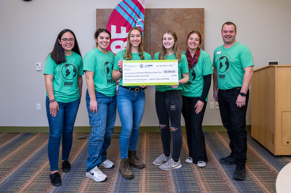 people in green shirts stand with a cardboard check 