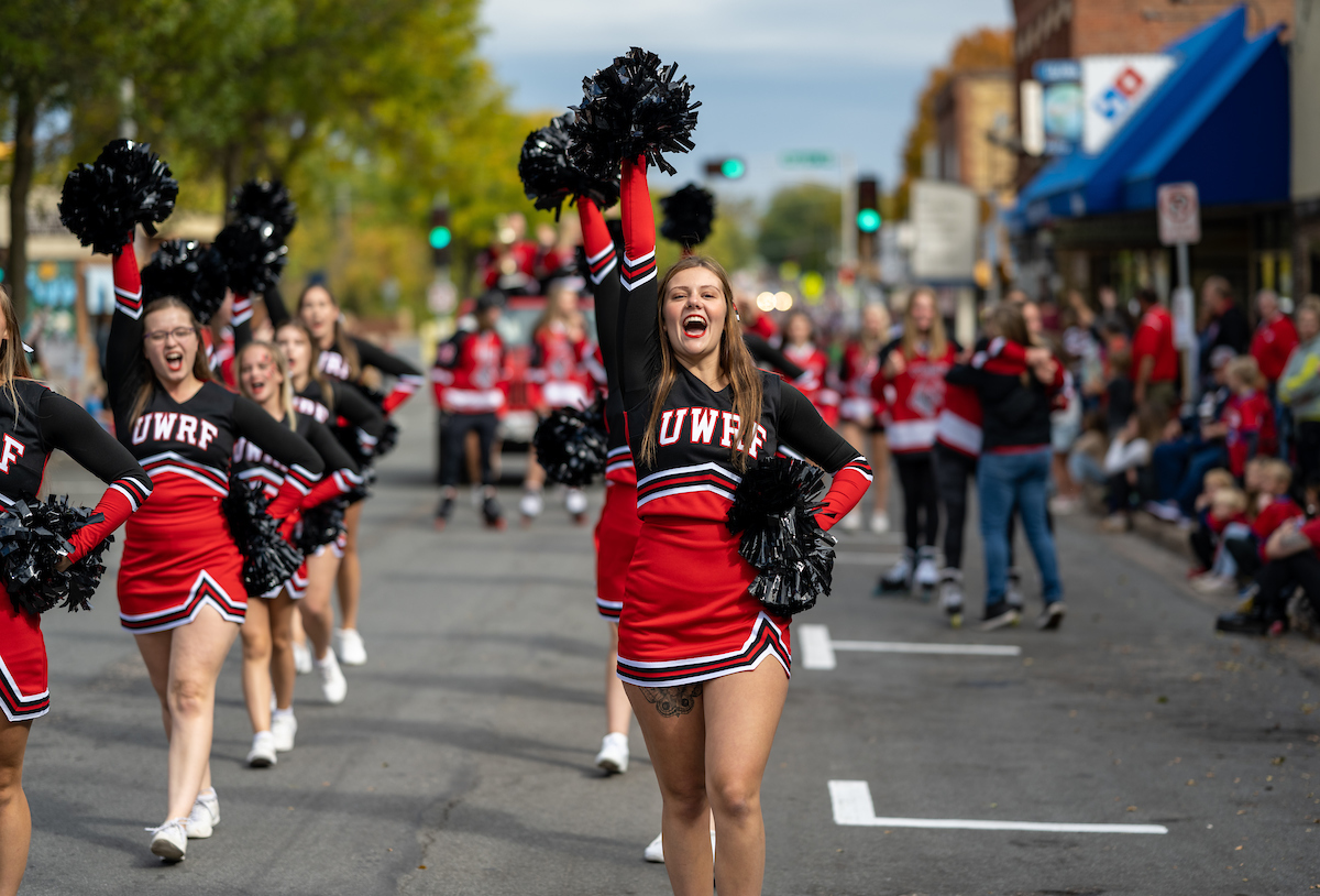 UWRF cheerleaders, wearing black and white uniforms and carrying black pompoms, walk down Main Street as part of the homecoming parade celebration