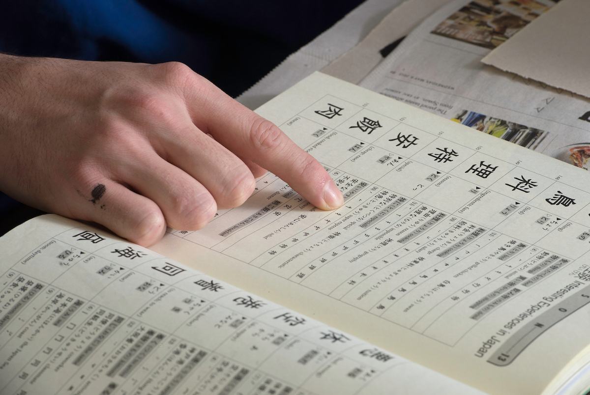 a hand points to a piece of paper with Japanese calligraphy on it