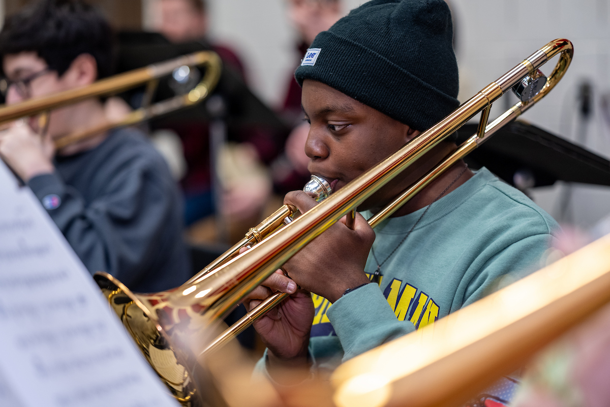 a male student wearing a blue shirt and black hat plays a trombone