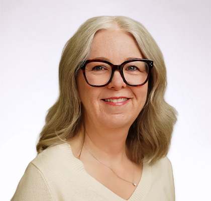 Headshot of Kelly Dunn, a middle aged woman with blonde hair and thick black rimmed glasses wearing a cream colored sweater