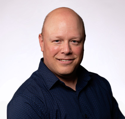 Headshot of Kevin Thaisen, a bald man wearing a dark blue button down shirt