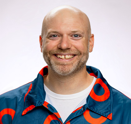 Headshot of Kevyn Juneau, a man wearing a blue and orange patterned button down shirt